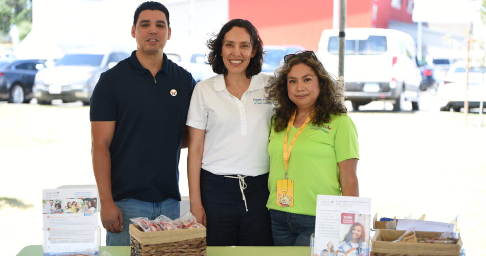 Health Plan of San Joaquin CEO Lizeth Granados standing with 2 employees as they smile behind a Health Plan of San Joaquin booth.