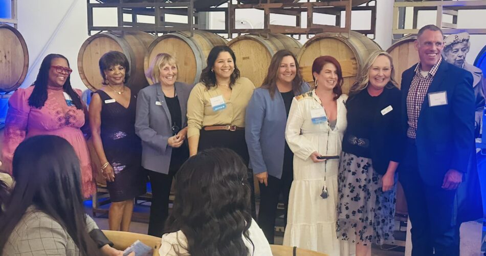 Women leaders from the Eleanor Women United event smiling in front of wooden barrels.
