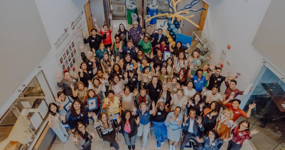 Health Plan of San Joaquin Employees and Providers gathered inside of the headquarters building. The image is shot from above looking down at everyone smiling and raising their hands.